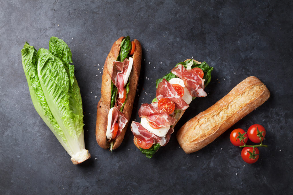 Ciabatta sandwich with romaine salad, prosciutto and mozzarella cheese over stone background.